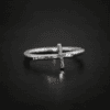 Close up of the "Creator" Ring. Made out of sterling silver. Ring has a thin, hammered oxidized cross going sideways across the ring band so that the top of the cross is on the right side of the ring band, the bottom of the cross is on the left side, and the two sides of the cross are sticking off of the ring band from the center of the cross. Ring is sitting against a dark background.